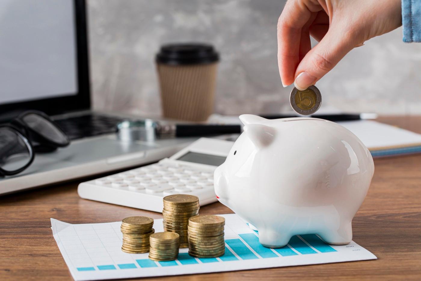 Hand placing a coin into a piggy bank beside growth charts